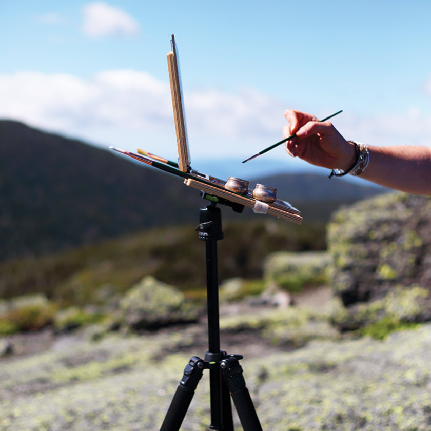 u.go Plein Air Anywhere Pochade Box, 8.4" x 11.25" model, on tripod showing thin side profile while plein air landscape painting